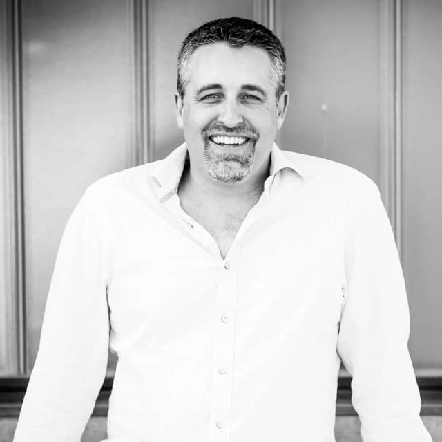 professional portrait of male entrepreneur Robert Evans in his 40s, adventure travel setting, natural warm lighting, approachable smile, outdoor trip attire, scenic nature background